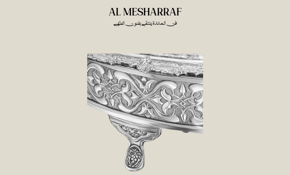 Decorative silver bowl with intricate patterns on a beige background, featuring the brand 'Al Mesharraf'.
